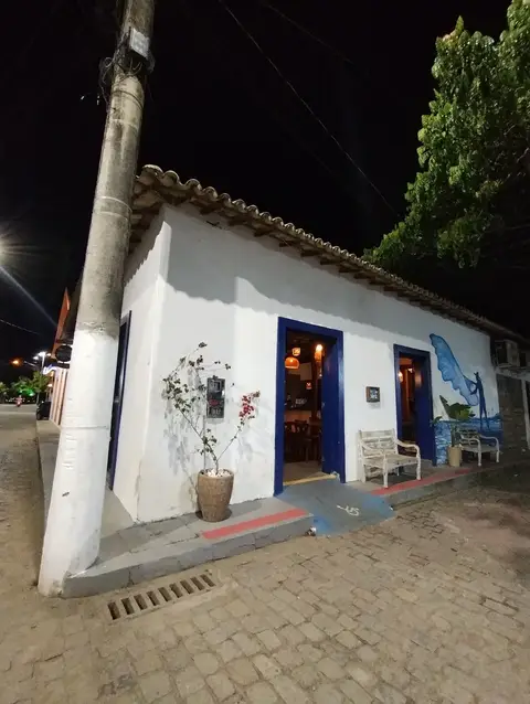 Fachada branca do casarão do Pirá à noite, com portas azuis abertas